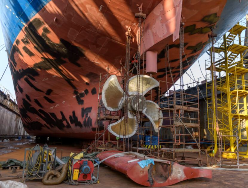 Cargo vessel in dry dock on ship repairing yard. Variable pitch propeller and rudder. Welder working on ship repairing yard.